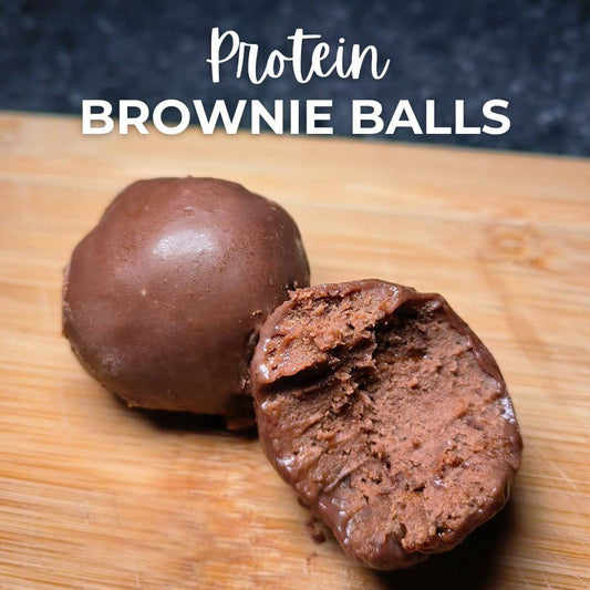 A chocolate brownie protein ball on a wooden surface, with one protein ball intact and the other broken open to show the inner texture.